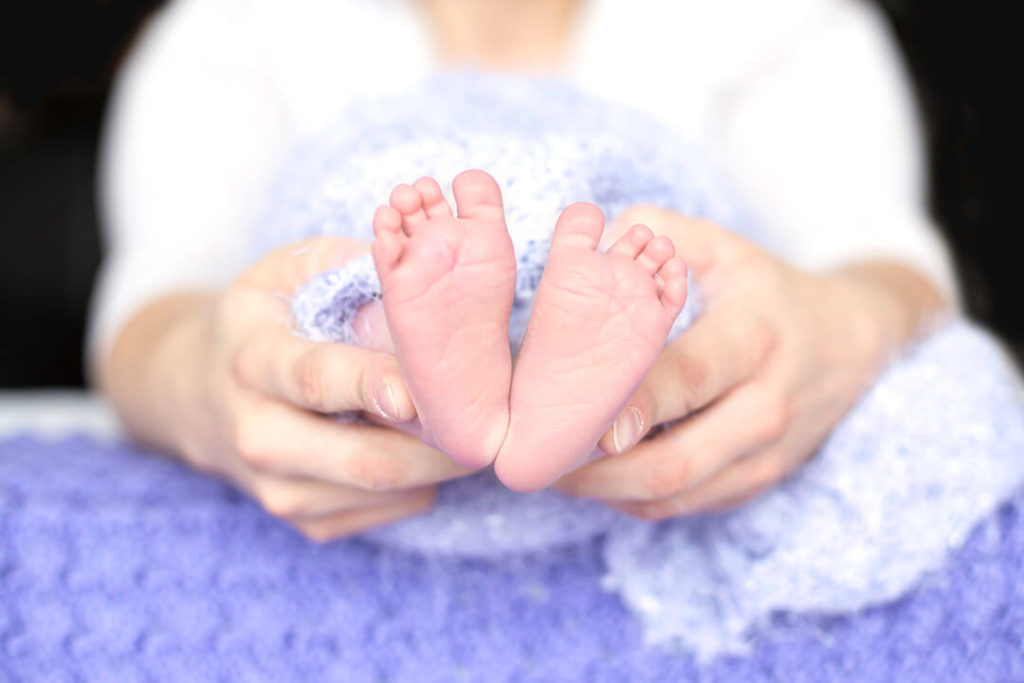 mother holding baby feet on purple background
