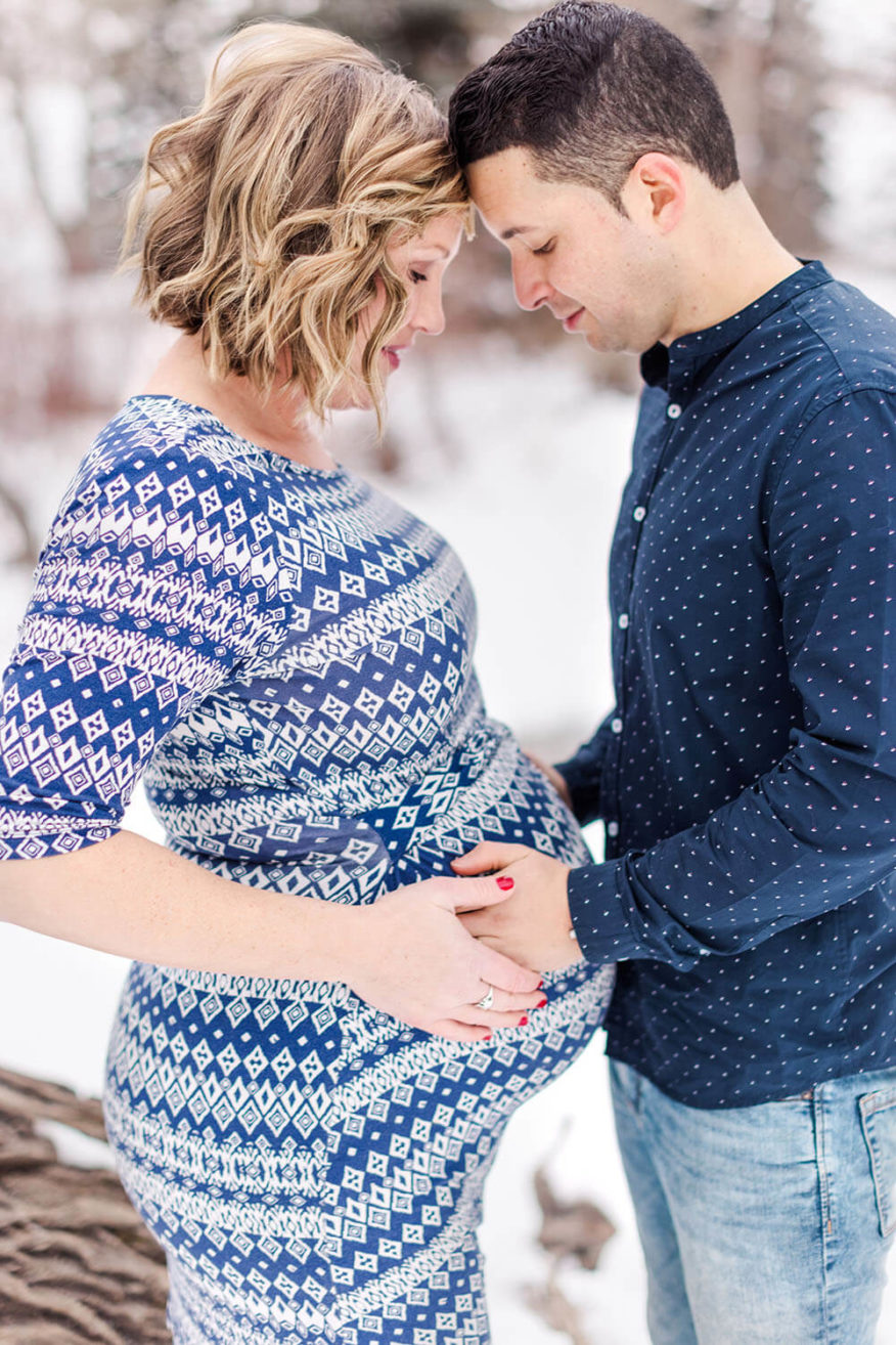 a woman with blonde short hair is looking down at her pregnant belly with her husband hold it as well.